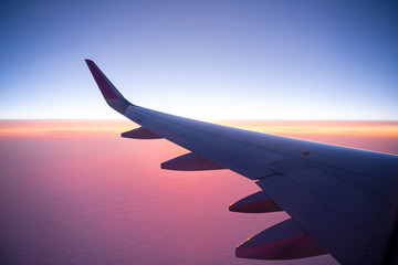 Fototapeta na wymiar Airplane wing in the sky above the clouds. Sunrise pink sky. Beautiful gentle clouds.