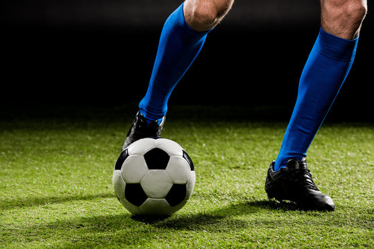 cropped view of sportsman playing with ball on green grass isolated on black