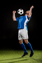 handsome football player in uniform jumping with ball isolated on black