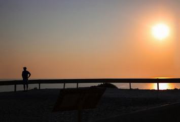 Sunset over the sea and road, traffic devider and dark silhouette of man with cap on his head,, Horizontal. Mideterranian, cyprus, road, ecology. With copy space