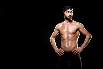Fototapeta na wymiar muscular swimmer standing in swimming cap and swim goggles isolated on black