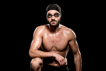 Fototapeta na wymiar muscular swimmer sitting in swimming cap and goggles isolated on black