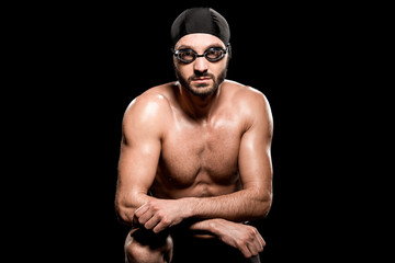 Fototapeta na wymiar handsome swimmer sitting in swimming cap and goggles isolated on black