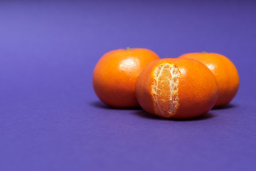 Three tangerines on purple background. Delicious mandarins with peel closeup.