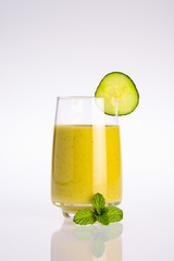 glass of green and yellow organic vegetable juice with slice of cucumber and mint leaf on white background