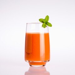 glass of orange organic vegetable juice with mint leaf on a white background