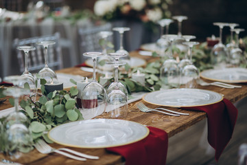 in the wedding banquet area there are tables and transparent chairs, on the tables there are plates, glasses, cutlery and compositions from green branches and candles