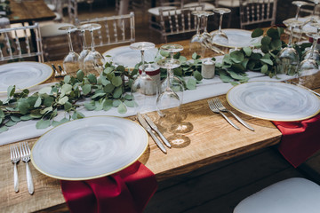 Fototapeta premium in the wedding banquet area there are tables and transparent chairs, on the tables there are plates, glasses, cutlery and compositions from green branches and candles