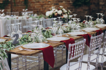 in the wedding banquet area there are tables and transparent chairs, on the tables there are plates, glasses, cutlery and compositions from green branches and candles
