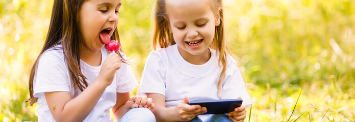 Two little sister girls playing internet with mobile smartphone on grass