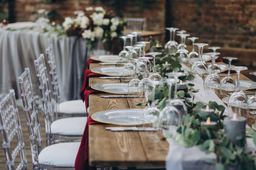 in the wedding banquet area there are tables and transparent chairs, on the tables there are plates, glasses, cutlery and compositions from green branches and candles