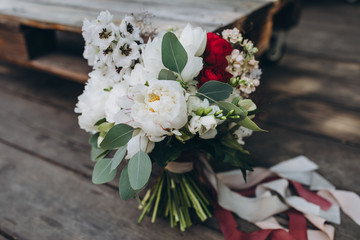 on the vintage floor of old wooden planks there is a bouquet of white flowers, red flowers, twigs and greenery tied with a ribbon