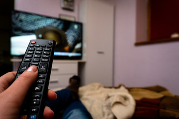 Female holding TV remote control in front of TV. Couch potatoe. Point of view shot.