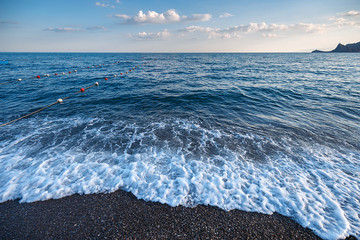 Summertime beach. Soft evening light reflecting on sea water and small waves with foam. Seascape.