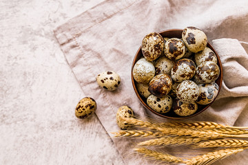 quail eggs in a wooden bowl on a table linen with ears of wheat on marble background