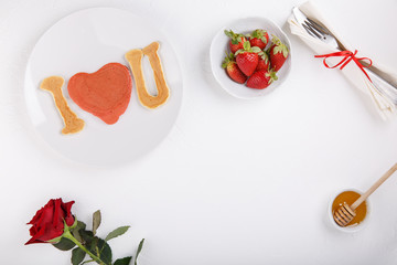 Heart shaped pancakes on white plate. I love you. Festive breakfast on white table. Love concept. Happy Valentine’s day. Top view.  Copy space.