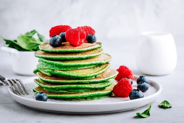 Healthy green spinach pancakes with raspberries, blueberries and honey