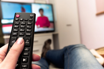 Female holding TV remote control in front of TV. Couch potatoe. Point of view shot.