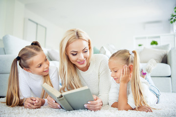 Fototapeta na wymiar Portrait of three nice-looking cute pretty lovely sweet attractive charming cheerful people pre-teen girls mom mommy lying on carpet reading novel in light white interior room house indoors