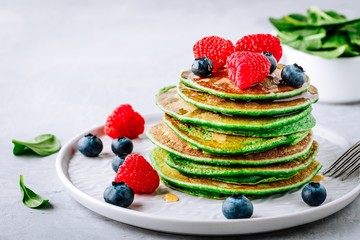 Healthy green spinach pancakes with raspberries, blueberries and honey