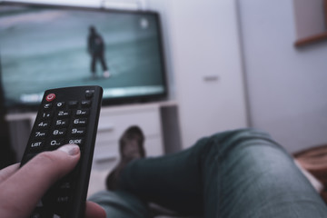 Female holding TV remote control in front of TV. Couch potatoe. Point of view shot.