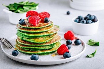 Healthy green spinach pancakes with raspberries, blueberries and honey