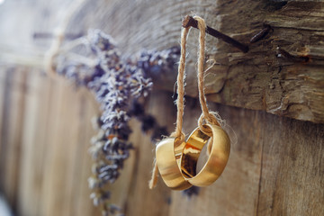 Hanging wedding rings and lavender flower on wooden wall