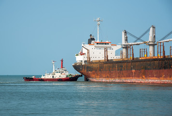 Fototapeta premium tug boat under pushing the ship to alongside the seaport terminal, docking yard, safety berthing the ship under navigating control by pilot and harbor master