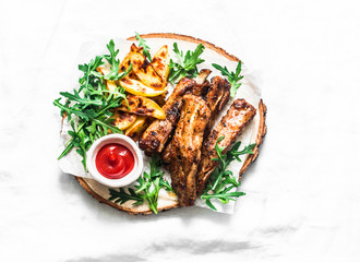 Grilled pork ribs and french fries on wooden board on light background top view. Delicious lunch, appetizers, tapas