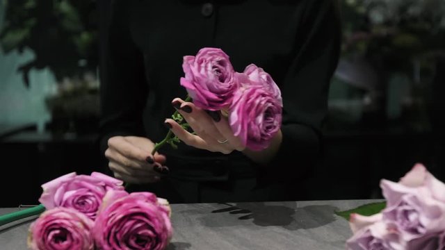 Professional florist cuts white and red roses with a pruner over the table, woman's hands close-up.