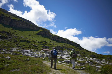 Fototapeta premium Elderly couple hiking up a mountain path in the Swiss Alps in summer sunshine