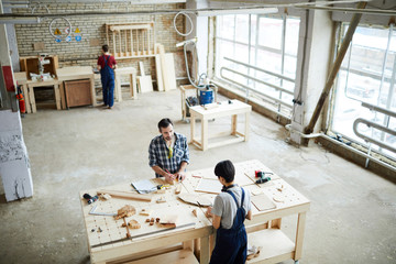 Carpentry workers standing at desk in spacious workshop and making wooden frames while producing goods for interior