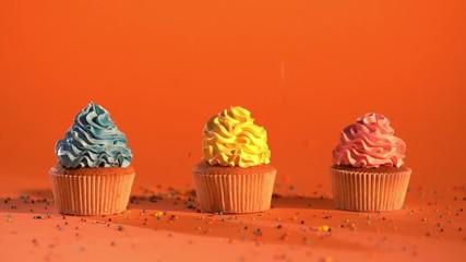 slow motion of sugary sprinkles falling down on multicolored cupcakes on orange background 