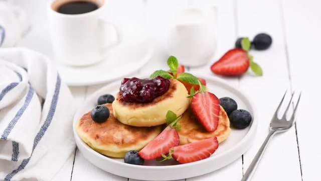 Pancakes or syrniki with fresh berries and jam on a plate. Putting breakfast plate on table