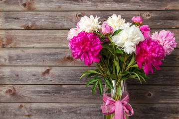 bouquet of pink and white peony flowers in a vase on a wooden ba
