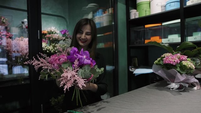 Professional woman florist makes the bouquet from pink flowers tulips, roses, orchids and solidago.