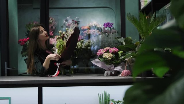 Florist holds in hand beautiful bouquet of flowers from Orchid Cymbidium, red and white roses and solidago in paper, hands close-up.