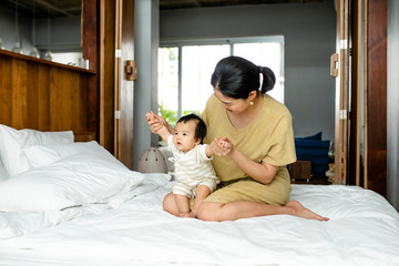 Beautiful Asian woman sitting on a bed and holding her baby.