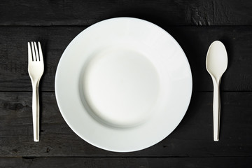 Empty white bowl, fork and spoon on black wood table, close-up view. Diet concept: flat lay of clean kitchen dishes on dark rustic background