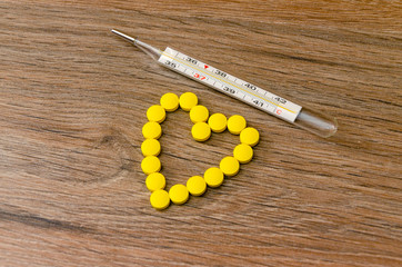 Small medical pharmaceptic round pills, vitamins, drugs in the form of a heart and  thermometer on a wood background. Concept: medicine, health care.