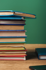 selective focus of stack with books on wooden table and green background
