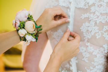 A bridesmaid helps a bride to wearing in wedding day morning close up