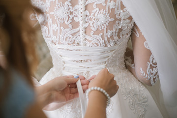 A bridesmaid helps a bride to wearing in wedding day morning close up