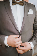 The groom fastens a jacket on wedding day morning close up