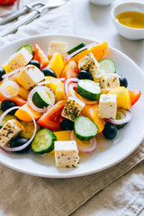 Greek salad of fresh cucumber, tomato, sweet pepper, red onion, feta cheese and olives with olive oil on marble.