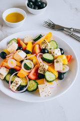 Greek salad of fresh cucumber, tomato, sweet pepper, red onion, feta cheese and olives with olive oil on marble.