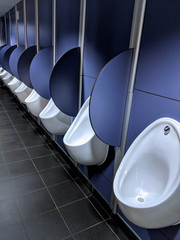 Row of shiny white porcelain urinals with purple medium density fibre board (MDF) fascia and stall...