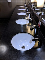 Row of shiny, contemporary, ceramic wash hand basins in front of a wall of top lit mirrors, in...