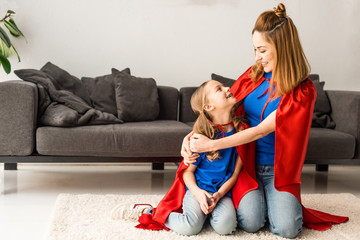 Kid and mother in red cloaks sitting on floor and looking at each other