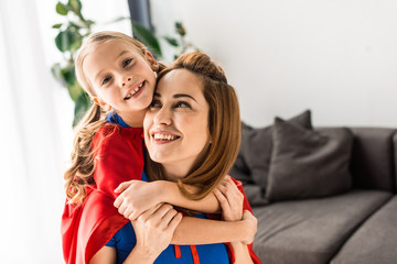 Cute daughter and mother in red cloaks hugging and smiling at home